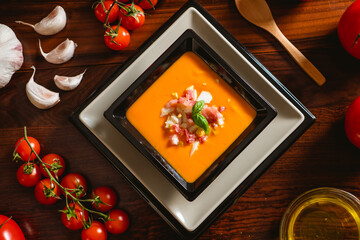 Receta típica española de salmorejo cordobés en un plato cuadrado y con algunos ingredientes al rededor.