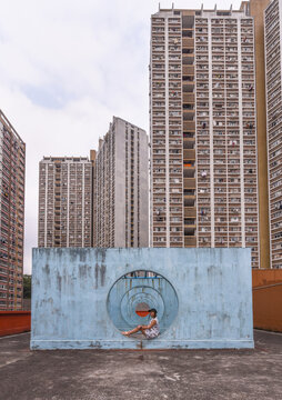 Female in summer dress sitting on concrete base of unusual city installation in shape of passage with round holes and looking away