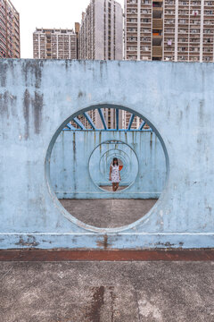 Female in summer dress standing on concrete base of unusual city installation in shape of passage with round holes and looking at camera
