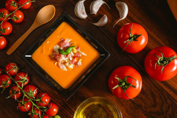 Receta típica española de salmorejo cordobés en un plato cuadrado y con algunos ingredientes al rededor.
