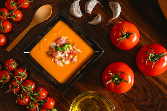 Receta t&iacute;pica espa&ntilde;ola de salmorejo cordob&eacute;s en un plato cuadrado y con algunos ingredientes al rededor.