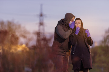 A man and a woman in hoods, in protective masks and purple gloves posing in the setting sun in the...
