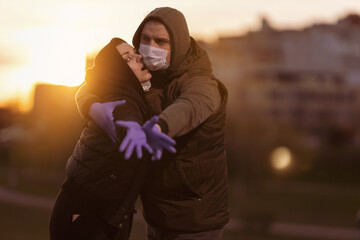 A man and a woman in hoods, in protective masks and purple gloves posing in the setting sun in the...