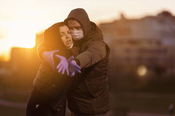 A man and a woman in hoods, in protective masks and purple gloves posing in the setting sun in the...