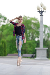 Girl ballerina in jeans, a plaid shirt and pointe shoes dancing in the city on the street © Tatiana
