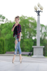 Girl ballerina in jeans, a plaid shirt and pointe shoes dancing in the city on the street © Tatiana
