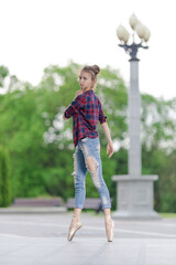 Girl ballerina in jeans, a plaid shirt and pointe shoes dancing in the city on the street © Tatiana