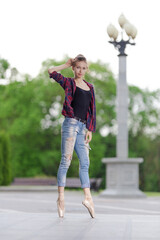 Girl ballerina in jeans, a plaid shirt and pointe shoes dancing in the city on the street © Tatiana