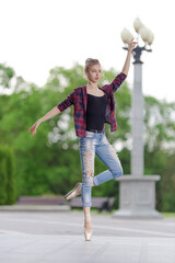 Girl ballerina in jeans, a plaid shirt and pointe shoes dancing in the city on the street © Tatiana