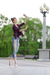 Girl ballerina in jeans, a plaid shirt and pointe shoes dancing in the city on the street © Tatiana