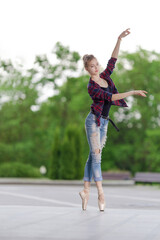 Girl ballerina in jeans, a plaid shirt and pointe shoes dancing in the city on the street © Tatiana