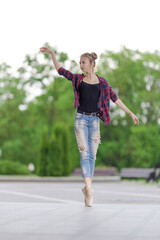 Girl ballerina in jeans, a plaid shirt and pointe shoes dancing in the city on the street © Tatiana