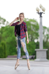 Girl ballerina in jeans, a plaid shirt and pointe shoes dancing in the city on the street © Tatiana