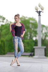Girl ballerina in jeans, a plaid shirt and pointe shoes dancing in the city on the street © Tatiana