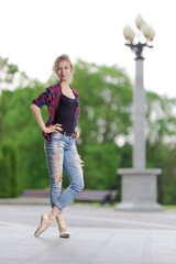 Girl ballerina in jeans, a plaid shirt and pointe shoes dancing in the city on the street © Tatiana