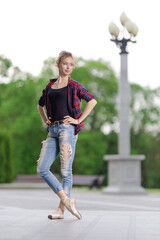 Girl ballerina in jeans, a plaid shirt and pointe shoes dancing in the city on the street © Tatiana