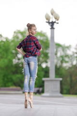 Girl ballerina in jeans, a plaid shirt and pointe shoes dancing in the city on the street © Tatiana