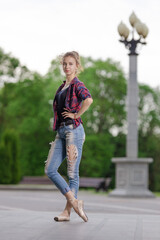 Girl ballerina in jeans, a plaid shirt and pointe shoes dancing in the city on the street © Tatiana