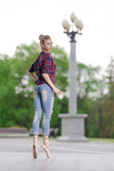 Girl ballerina in jeans, a plaid shirt and pointe shoes dancing in the city on the street © Tatiana