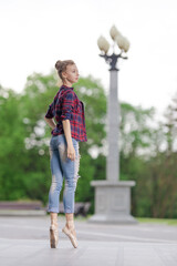 Girl ballerina in jeans, a plaid shirt and pointe shoes dancing in the city on the street © Tatiana