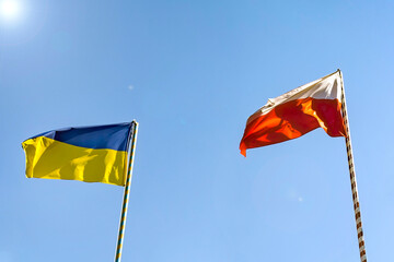 Flags of Ukraine and Poland. Two flags on the background of a beautiful blue sky and trees. - 358591285