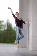 Girl ballerina in jeans, a plaid shirt and pointe shoes dancing in the city on the street © Tatiana