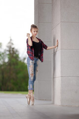 Girl ballerina in jeans, a plaid shirt and pointe shoes dancing in the city on the street © Tatiana
