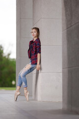 Girl ballerina in jeans, a plaid shirt and pointe shoes dancing in the city on the street © Tatiana