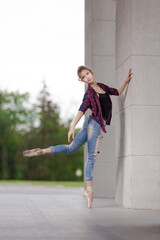 Girl ballerina in jeans, a plaid shirt and pointe shoes dancing in the city on the street © Tatiana