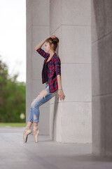 Girl ballerina in jeans, a plaid shirt and pointe shoes dancing in the city on the street © Tatiana