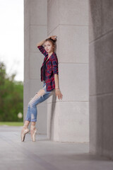 Girl ballerina in jeans, a plaid shirt and pointe shoes dancing in the city on the street © Tatiana