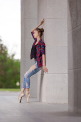 Girl ballerina in jeans, a plaid shirt and pointe shoes dancing in the city on the street © Tatiana