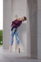 Girl ballerina in jeans, a plaid shirt and pointe shoes dancing in the city on the street © Tatiana