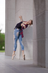 Girl ballerina in jeans, a plaid shirt and pointe shoes dancing in the city on the street © Tatiana
