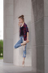 Girl ballerina in jeans, a plaid shirt and pointe shoes dancing in the city on the street © Tatiana