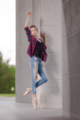 Girl ballerina in jeans, a plaid shirt and pointe shoes dancing in the city on the street © Tatiana