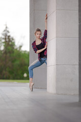 Girl ballerina in jeans, a plaid shirt and pointe shoes dancing in the city on the street © Tatiana
