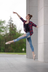 Girl ballerina in jeans, a plaid shirt and pointe shoes dancing in the city on the street © Tatiana