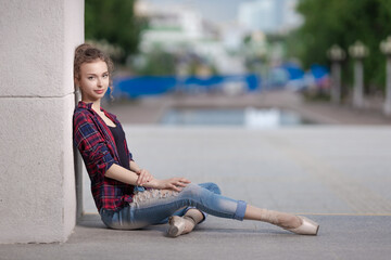 Girl ballerina in jeans, a plaid shirt and pointe shoes dancing in the city on the street © Tatiana