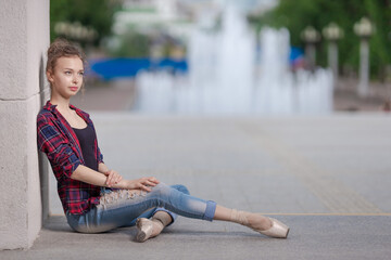 Girl ballerina in jeans, a plaid shirt and pointe shoes dancing in the city on the street © Tatiana