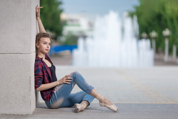 Girl ballerina in jeans, a plaid shirt and pointe shoes dancing in the city on the street © Tatiana