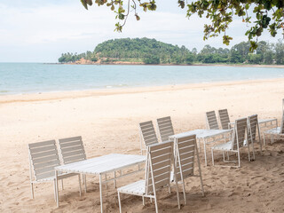 White tables under trees on the beach. Copy space provided.