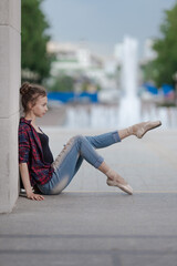 Girl ballerina in jeans, a plaid shirt and pointe shoes dancing in the city on the street © Tatiana