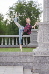 Girl ballerina in jeans, a plaid shirt and pointe shoes dancing in the city on the street © Tatiana
