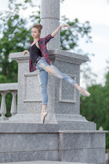 Girl ballerina in jeans, a plaid shirt and pointe shoes dancing in the city on the street © Tatiana