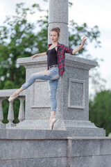Girl ballerina in jeans, a plaid shirt and pointe shoes dancing in the city on the street © Tatiana