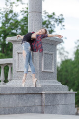 Girl ballerina in jeans, a plaid shirt and pointe shoes dancing in the city on the street © Tatiana