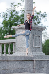 Girl ballerina in jeans, a plaid shirt and pointe shoes dancing in the city on the street © Tatiana