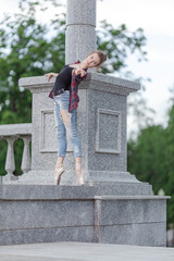 Girl ballerina in jeans, a plaid shirt and pointe shoes dancing in the city on the street © Tatiana