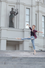 Girl ballerina in jeans, a plaid shirt and pointe shoes dancing in the city on the street © Tatiana